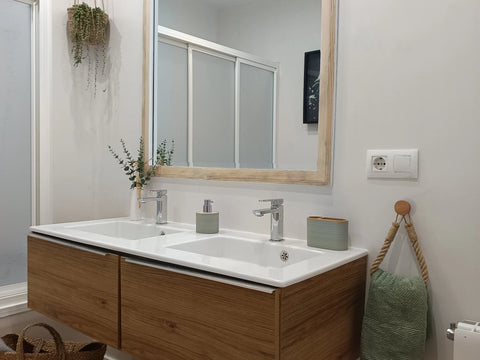 Paredes de baño en microcemento blanco con lavabo doble, espejo grande y mueble de madera natural.