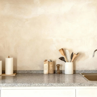 Pared de cocina revestida con microcemento color Porcelain y encimera de granito con utensilios de madera.
