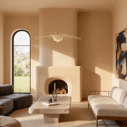 Chimenea de obra en microcemento color India con formas suaves en salón luminoso con ventanal arqueado, mesa de piedra y sofás neutros.