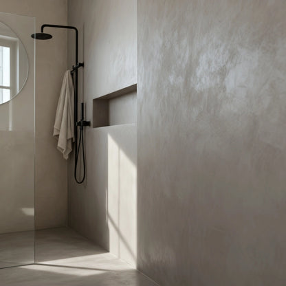 Ducha de obra en microcemento color Universe con grifería negra, hornacina integrada y luz natural entrando por la ventana.