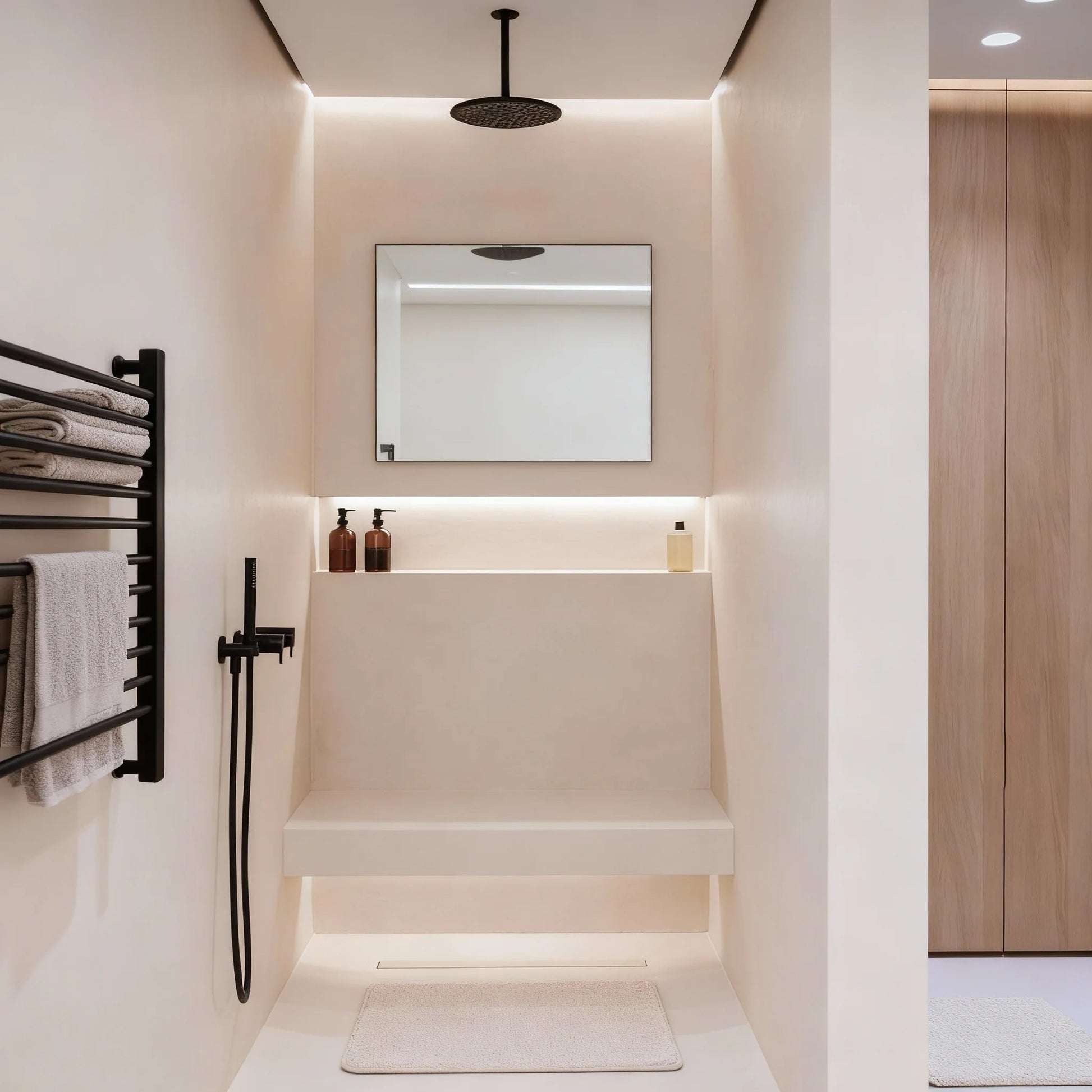 Ducha de obra con microcemento color Blanco Roto con banco integrado, grifería negra y luz indirecta cálida.