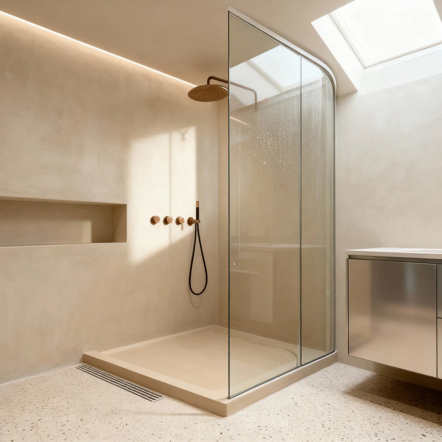Ducha de obra con microcemento color Bone con hornacina alargada y mampara curva, iluminada por lucernario.
