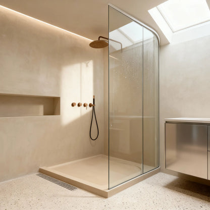 Ducha de obra con microcemento color Bone con hornacina alargada y mampara curva, iluminada por lucernario.