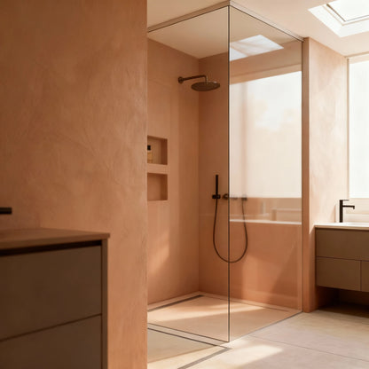 Baño con ducha de obra acristalada en microcemento color Café, grifería negra y luz natural que entra desde la ventana.