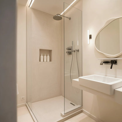 Ducha recubierta con microcemento color Porcelain, con mampara de cristal y grifería cromada en un baño luminoso y minimalista.