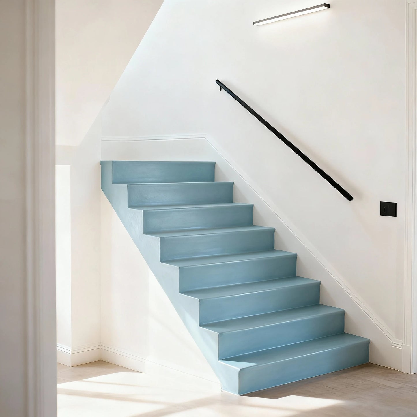 Escalera de obra decorada con microcemento color Breeze, barandilla negra minimalista y luz artificial en el lateral.