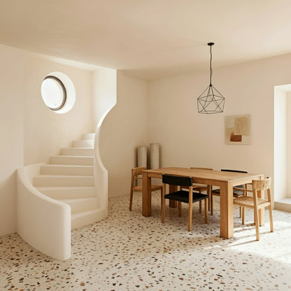 Comedor luminoso con escalera curva de obra en microcemento Blanco, mesa de madera y suelo de terrazo.