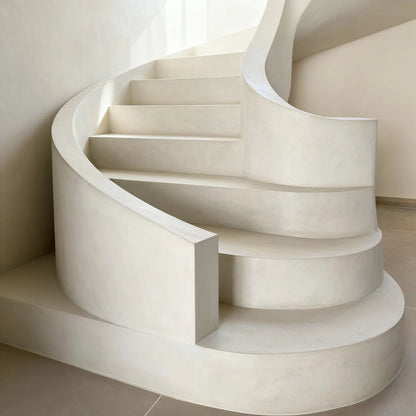 Escalera curva de microcemento color Blanco Roto con pasamanos continuo y formas orgánicas.