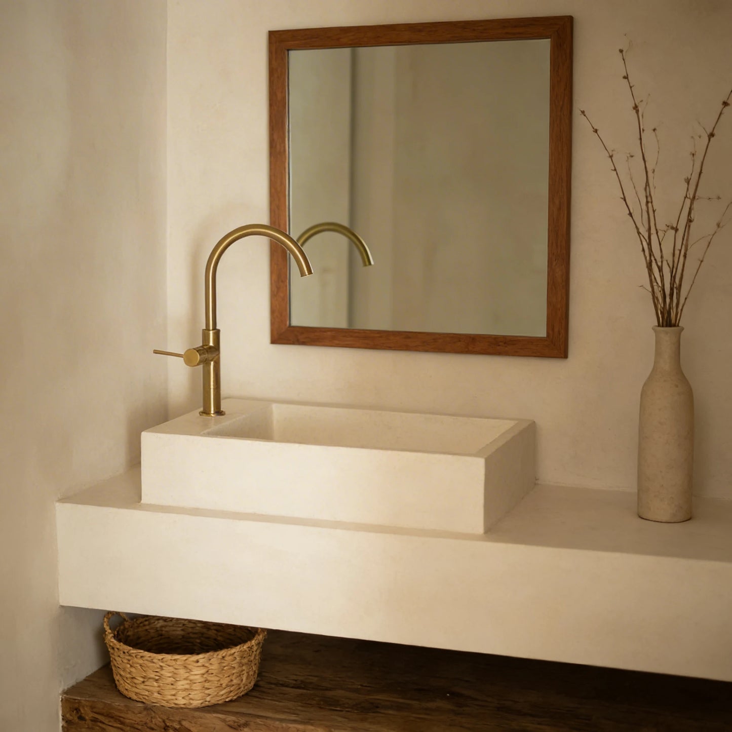 Lavabo de microcemento de dos alturas en color Porcelain con grifería dorada, en un aseo con espejo con marco de madera y balda inferior con cesta de mimbre.
