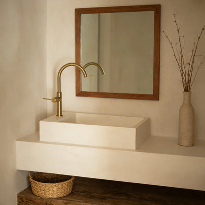 Lavabo de microcemento de dos alturas en color Porcelain con grifería dorada, en un aseo con espejo con marco de madera y balda inferior con cesta de mimbre.