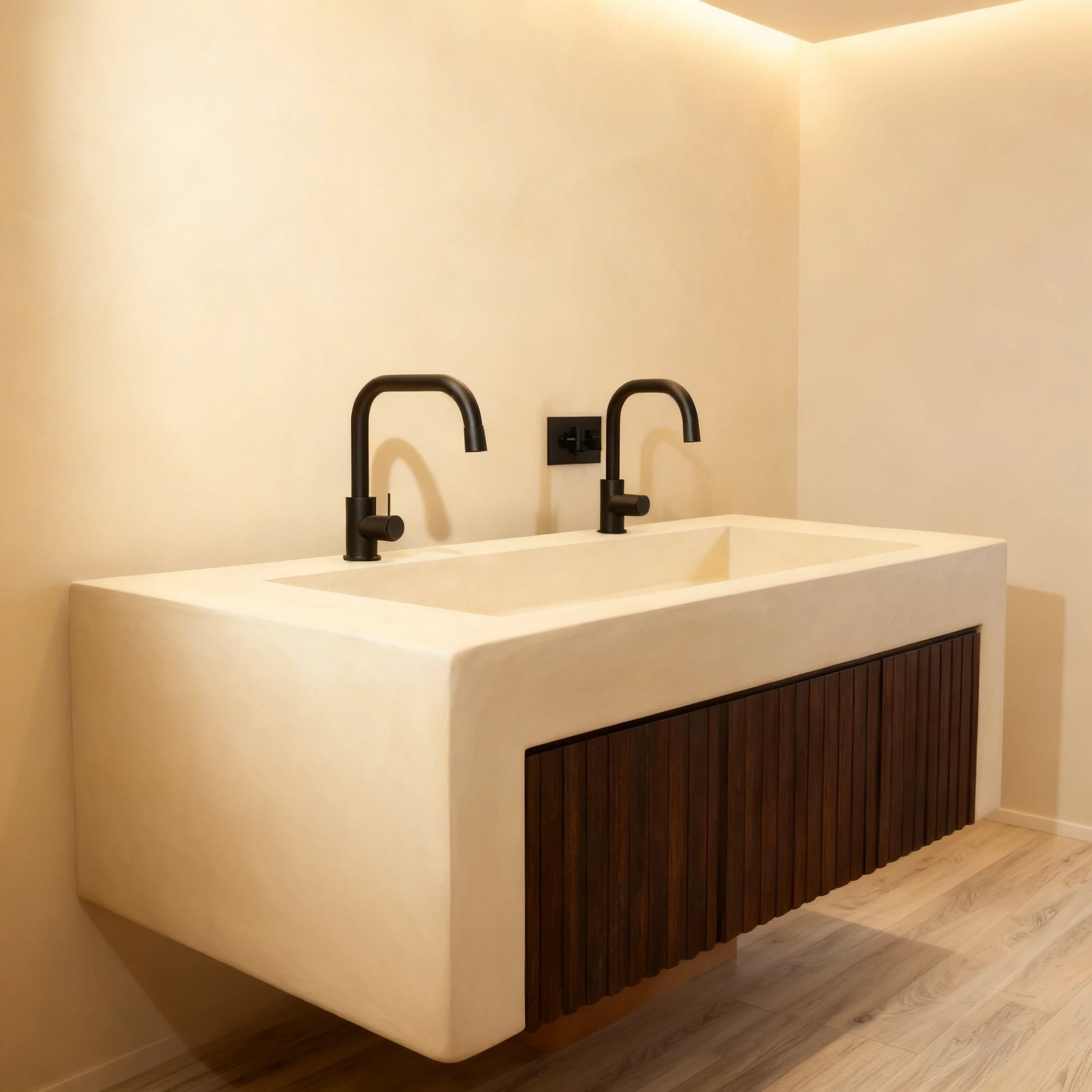 Lavabo suspendido de microcemento en color Champagne, con grifería negra y frontal de madera oscura, en un baño minimalista con suelo efecto madera.
