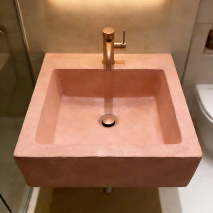 Lavabo cuadrado de microcemento en color Salmón,  equipado con grifería y desagüe central cobre, en un baño de estilo contemporáneo.