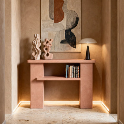 Consola de microcemento en color Blush con balda central, situada en un recibidor con paredes en tonos cálidos y suelo de piedra natural. 