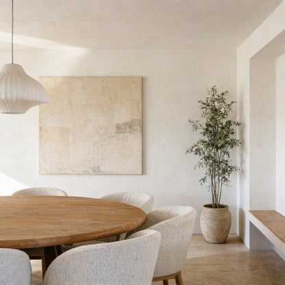 Comedor minimalista con paredes de microcemento color Blanco, mesa redonda de madera maciza natural y sillas tapizadas en tela bouclé beige. 