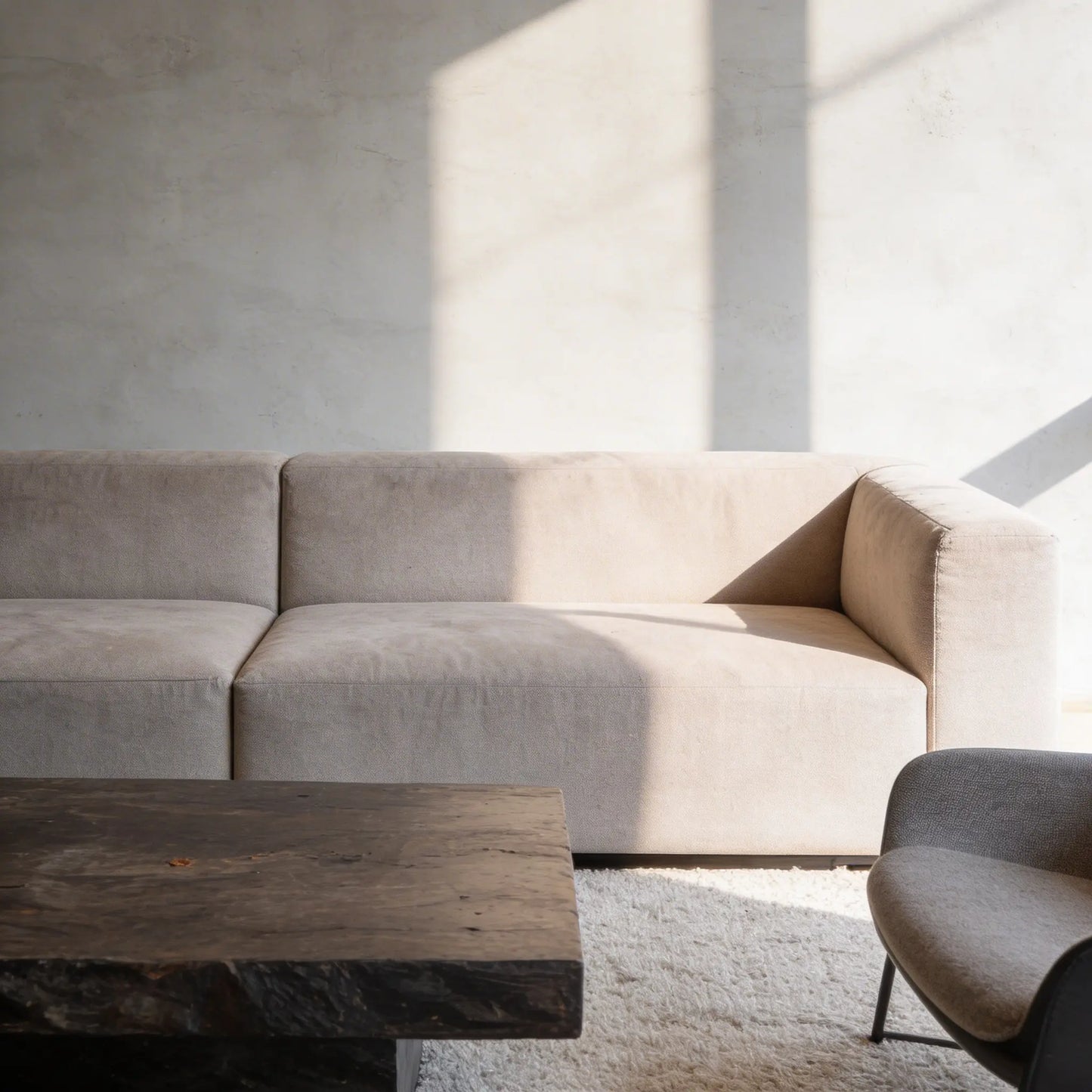 Salón contemporáneo con pared de microcemento gris color Universe, iluminadopor luz natural lateral y mesa de roble macizo.