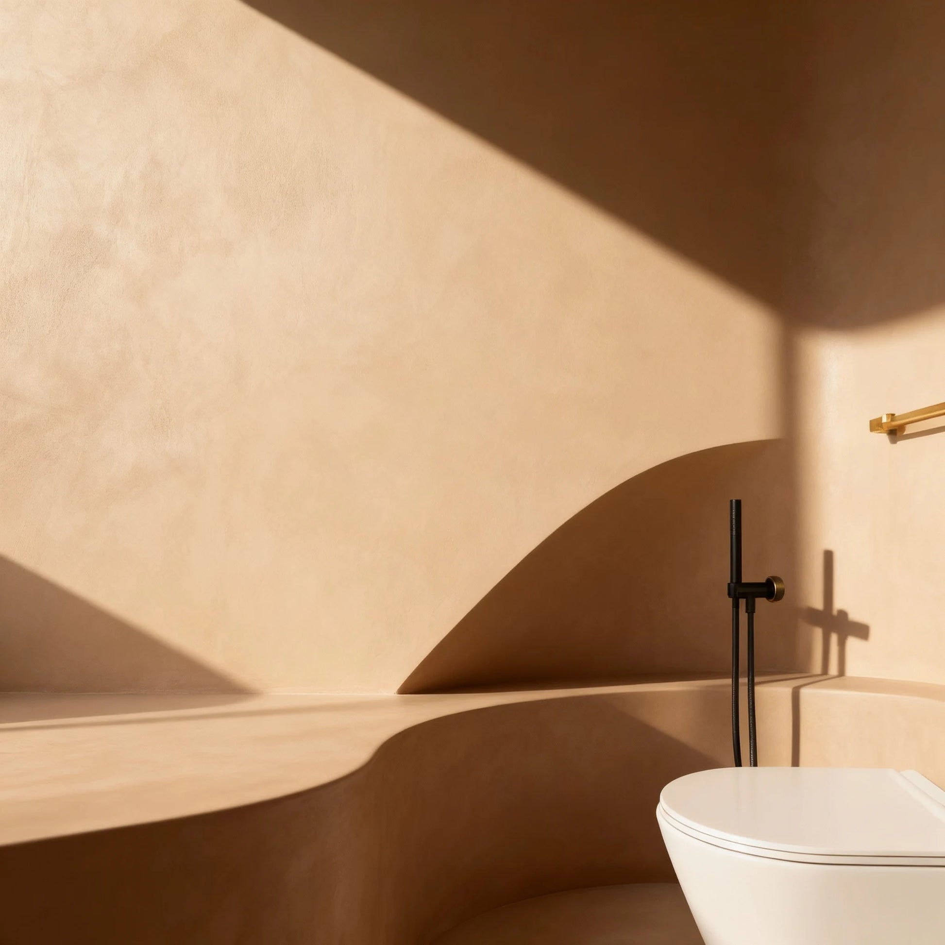 Baño con paredes de microcemento color Mojave con formas curvas, luz cálida y grifería negra.