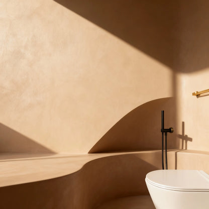 Baño con paredes de microcemento color Mojave con formas curvas, luz cálida y grifería negra.