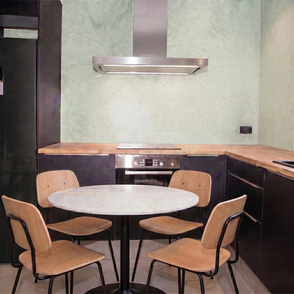 Cocina moderna con paredes de microcemento Smartcret color Moss, muebles negros, encimera de madera y mesa redonda con sillas.