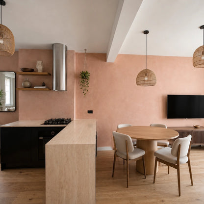 Cocina americana con paredes de microcemento Smartcret color Salmón, isla central, lámparas de mimbre, mesa redonda de madera y salón integrado.