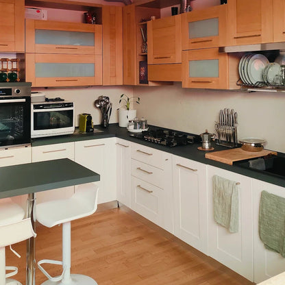 Cocina renovada con salpicadero de microcemento Smartcret color Bone, mobiliario blanco y encimera negra.