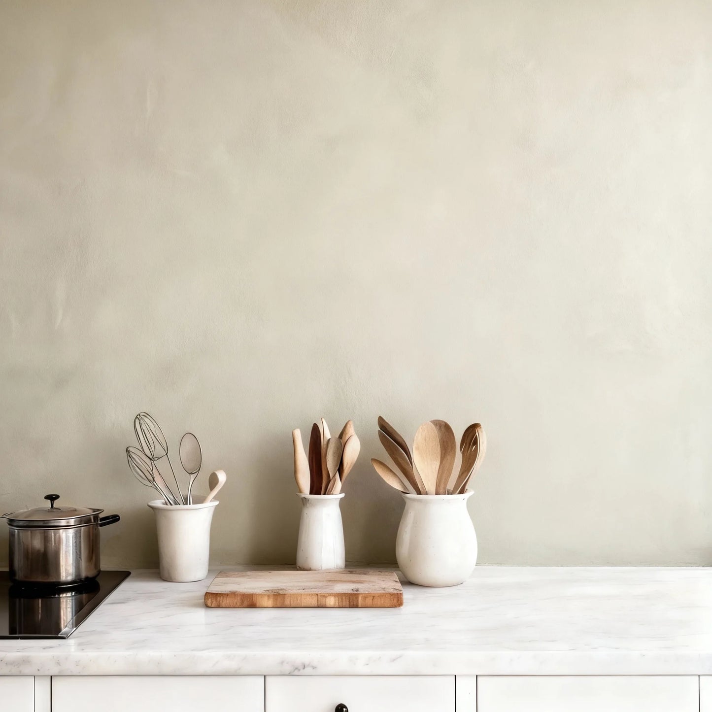 Pared de cocina en microcemento color Liquen con encimera blanca y utensilios de madera organizados sobre la superficie.