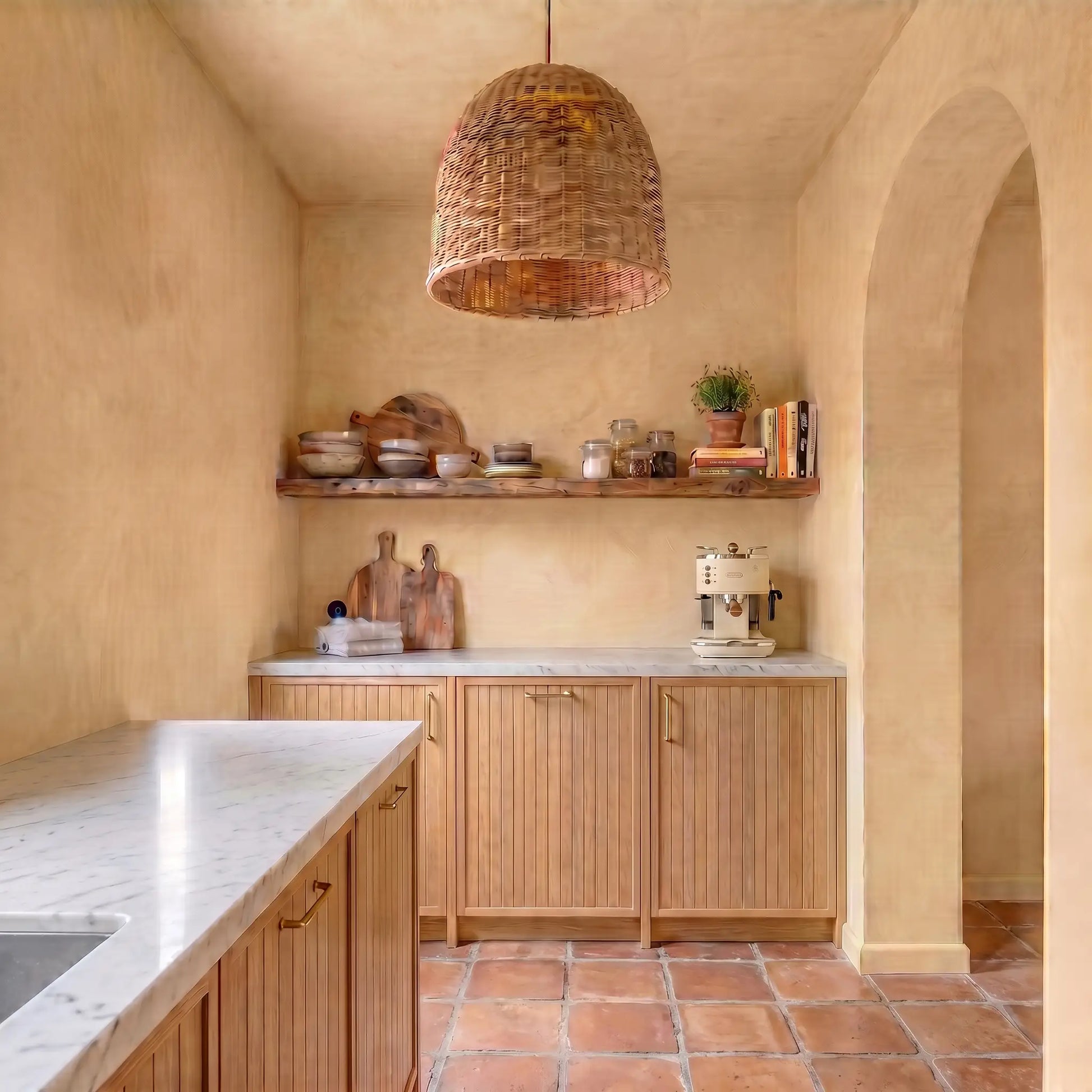 Amplia cocina con paredes de microcemento Smartcret color India, muebles de madera natural, encimera clara, lámpara de mimbre y suelo cerámico en tono terracota.