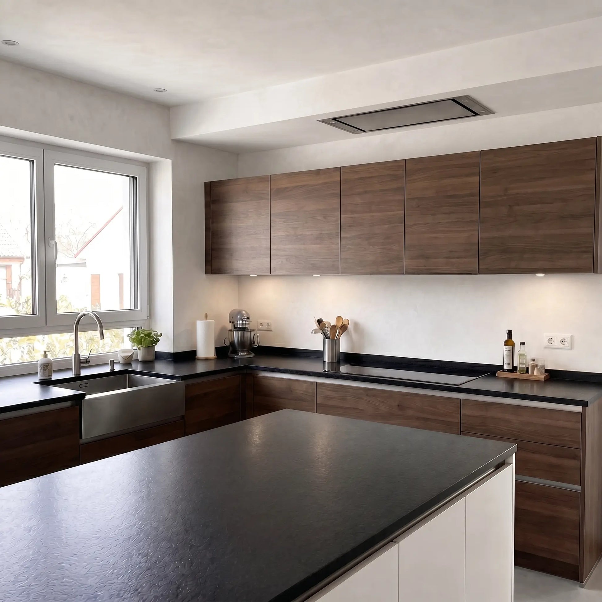 Cocina moderna con paredes de microcemento Blanco de Smartcret, acabado continuo de textura suave, muebles de madera, encimera negra e isla central.