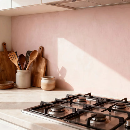 Pared de cocina en microcemento color Blush iluminada por luz natural, con encimera clara y utensilios de madera apoyados sobre el tablero.
