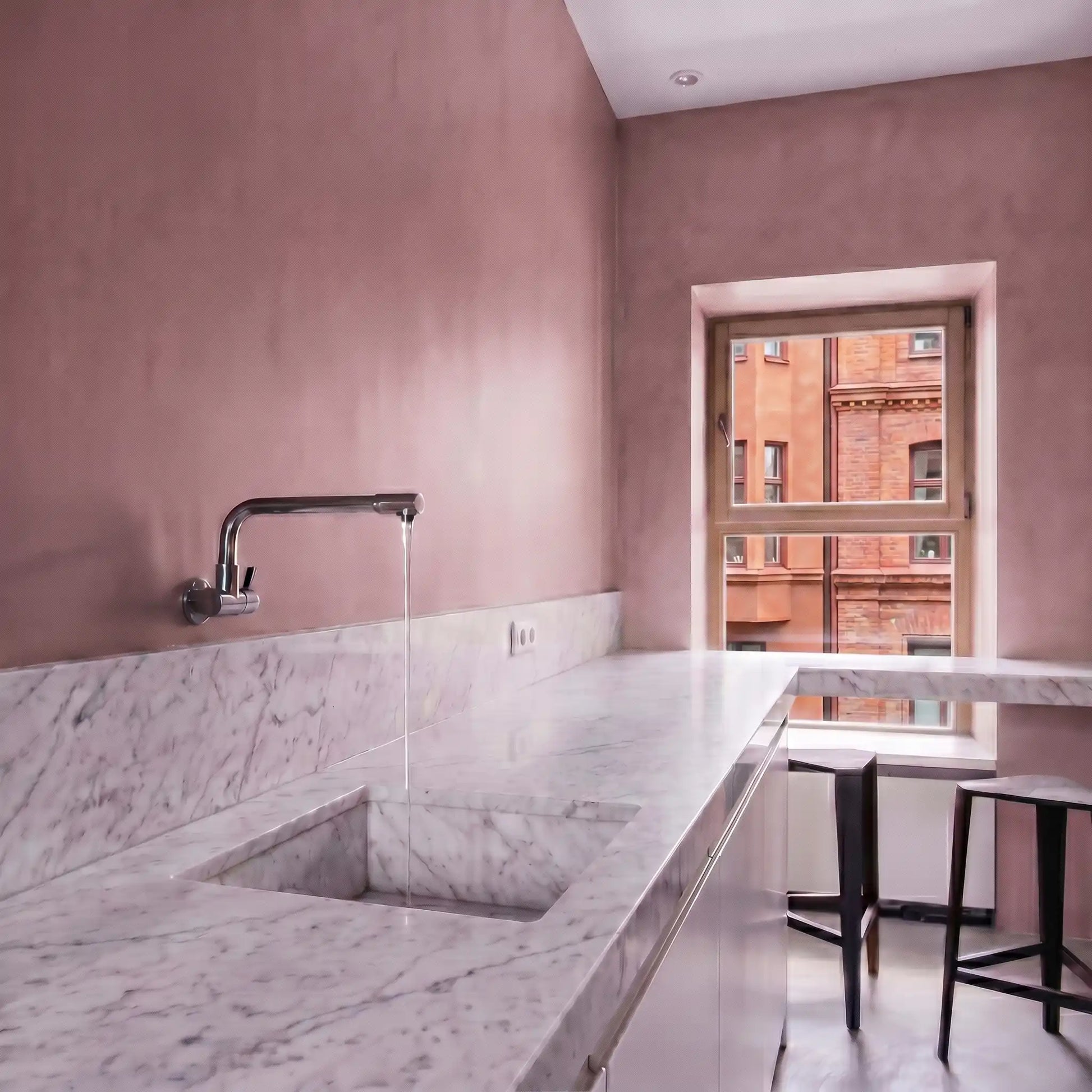 Vivienda tipo loft con paredes de microcemento en la cocina color Blush, encimera de mármol blanco, grifo mural y ventana con luz natural.