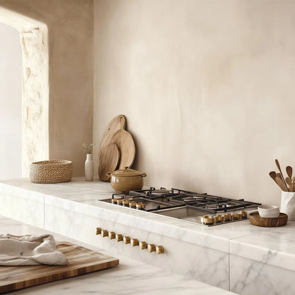  Pared de cocina de microcemento color Porcelain, encimera de mármol y luz cálida sobre detalles de madera.