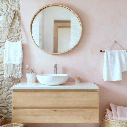 Pared de baño en microcemento color Blush con lavabo blanco, mueble de madera clara y detalles naturales en un ambiente suave.