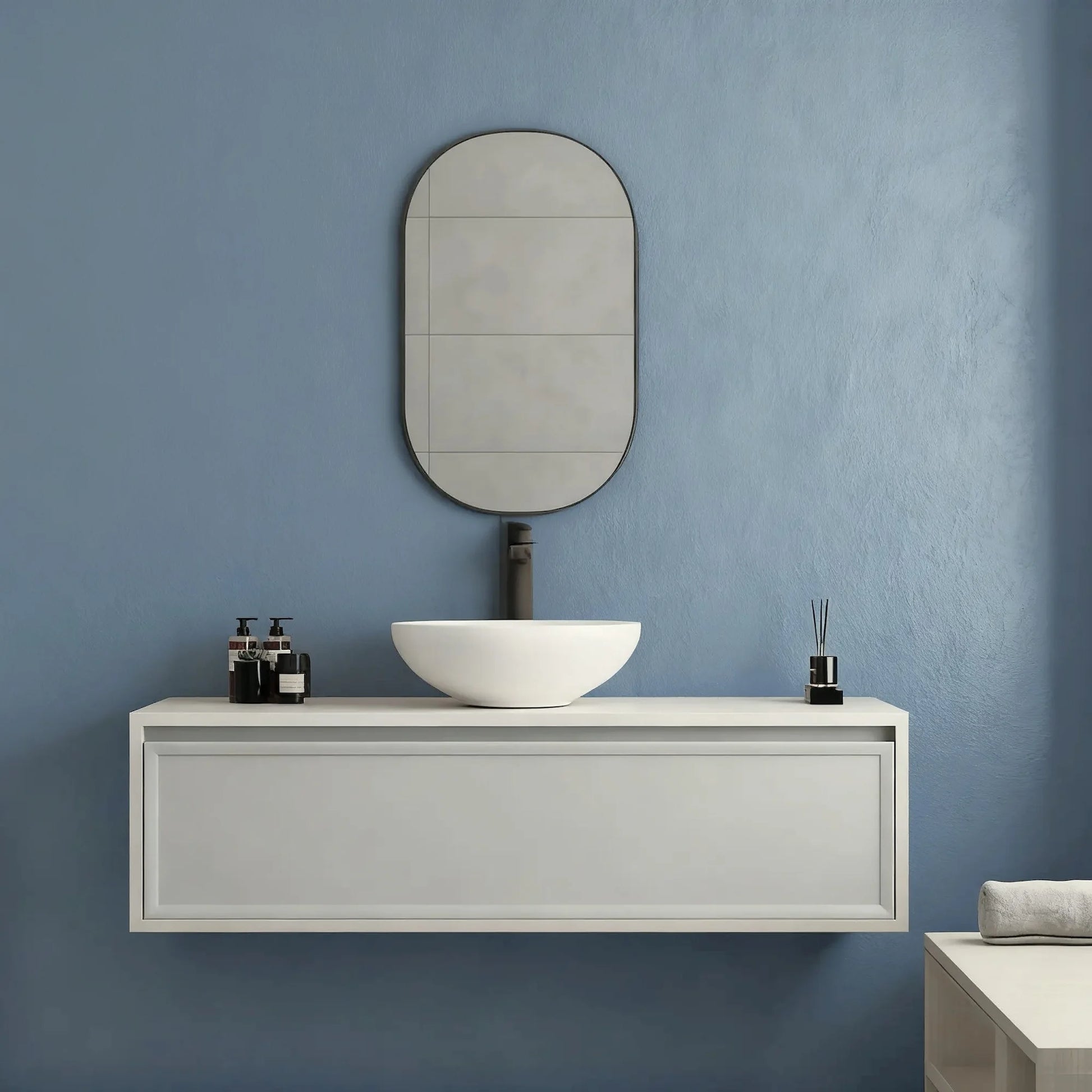  Pared de baño en microcemento color Breeze con lavabo blanco, mueble minimalista y detalles en negro en un ambiente sereno.