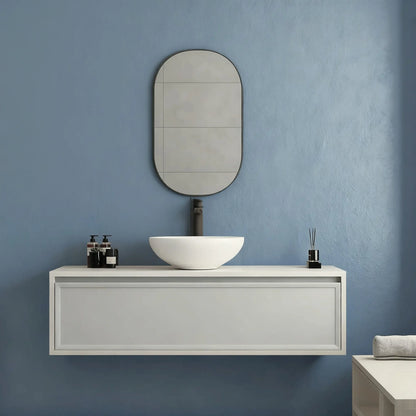  Pared de baño en microcemento color Breeze con lavabo blanco, mueble minimalista y detalles en negro en un ambiente sereno.