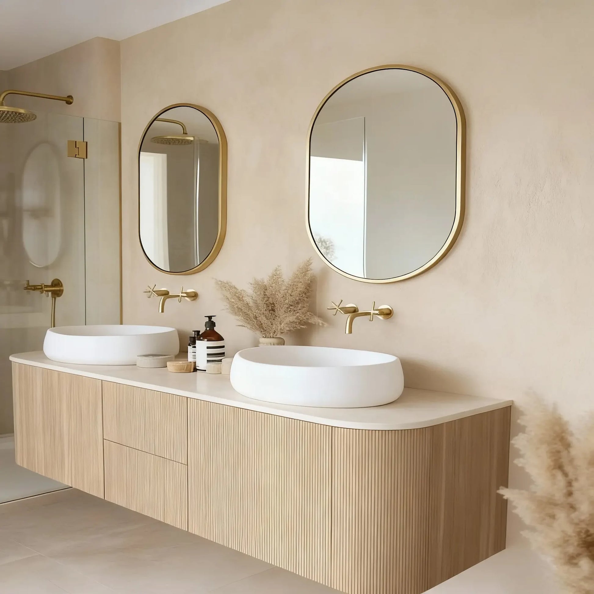 Pared de baño en microcemento color Champagne con doble lavabo blanco, muebles de madera clara y detalles dorados.