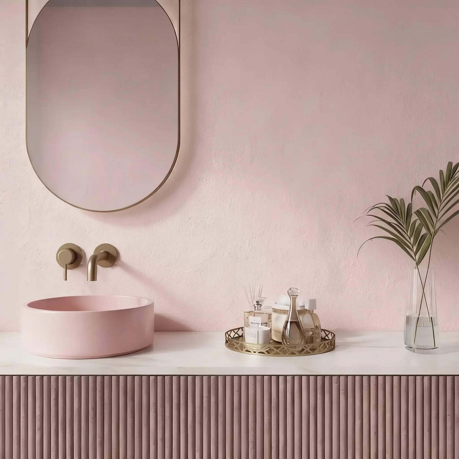 Pared de baño en microcemento color Blush con lavabo rosa, muebles estriados y detalles dorados en un ambiente suave y elegante.