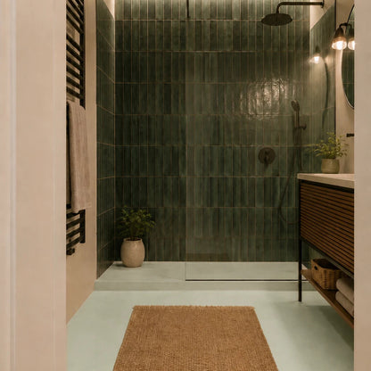 Baño moderno con suelo de microcemento verde color Moss, ducha frontal con azulejos verdes, mueble de madera y alfombra de yute.
