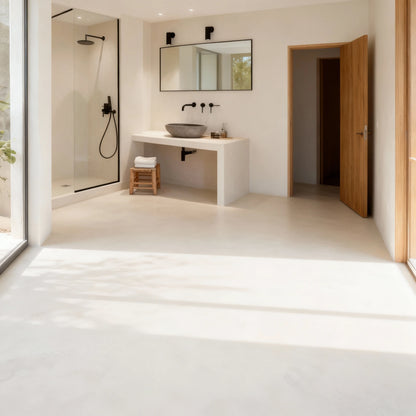 Amplio baño con suelo de microcemento color Blanco Roto, ducha al fondo y lavabo sobre un mueble minimalista en el mismo acabado.