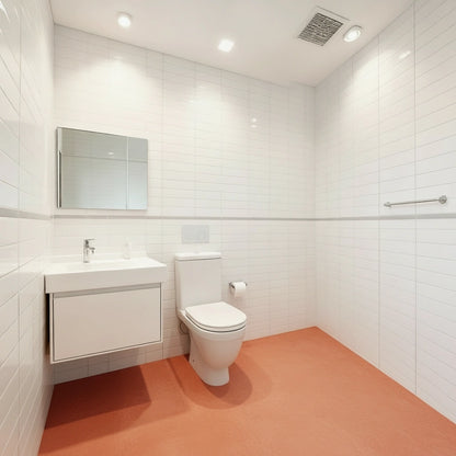 Baño pequeño con suelo de microcemento color Coral que aporta un contraste frente al alicatado blanco de las paredes.