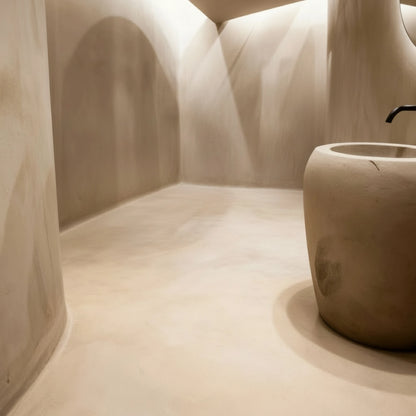 Baño de estilo orgánico con suelo de microcemento color Bone y un lavabo escultórico de líneas redondeadas que aporta un aire artesanal.