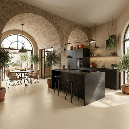 Cocina de estilo mediterráneo con pavimento de microcemento beige color Champagne, isla central oscura, paredes de piedra y zona de comedor luminosa.