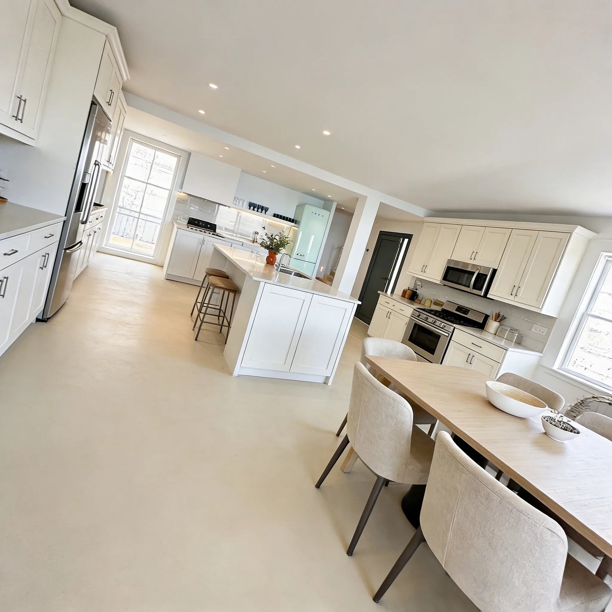 Cocina abierta al salón con isla central, suelo de microcemento en tono crema color Porcelain de Smartcret y comedor integrado con mesa de madera.