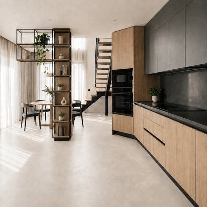 Dúplex con cocina abierta al comedor, suelo de microcemento color Blanco Roto, mobiliario de madera clara, armarios negros, estantería decorativa y escalera que conecta con el piso superior.