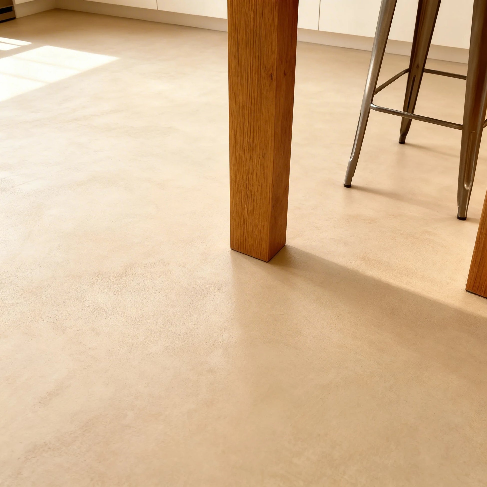 Suelo de microcemento beige color India de Smartcret en cocina, junto a mesa de madera y taburete metálico.