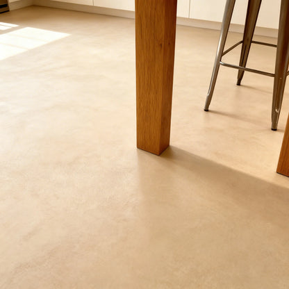 Suelo de microcemento beige color India de Smartcret en cocina, junto a mesa de madera y taburete metálico.