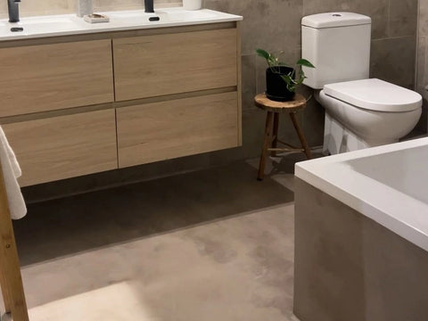 Suelo de microcemento en baño moderno con mueble de madera suspendido.